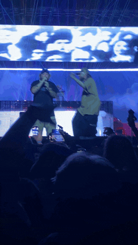 two men are singing into microphones in front of a large screen that says ' fame ' on it