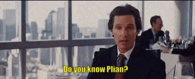 a man in a suit and tie is sitting at a table and says do you know plian