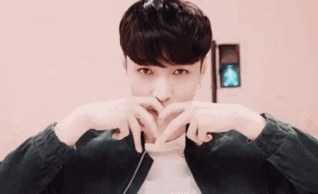 a young man is making a heart shape with his hands over his mouth .