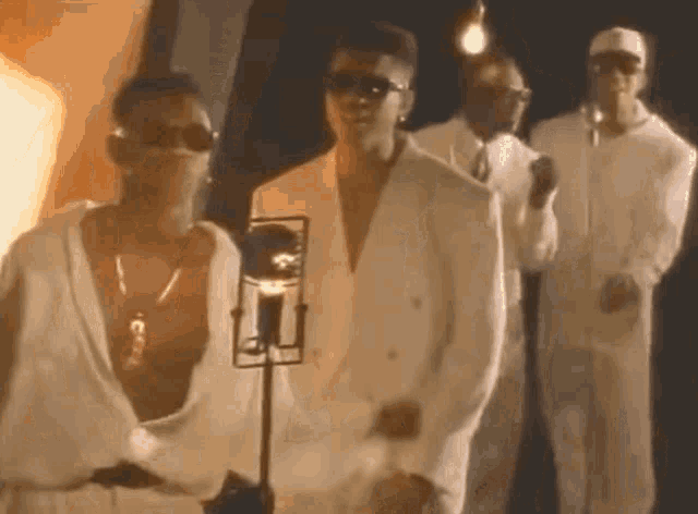a group of men in white suits and sunglasses are standing next to each other in front of a microphone .