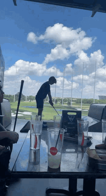 a man is swinging a golf club on a golf course behind a table with drinks