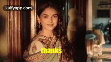 a woman in a green saree is smiling and standing in a doorway .