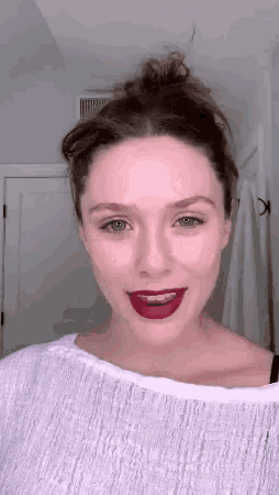 a woman wearing a white shirt and red lipstick is smiling