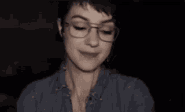 a woman with short hair and glasses is covering her mouth with her hands .