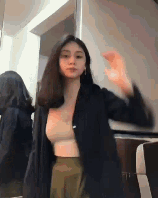 a woman is dancing in front of a mirror in a room while wearing a crop top and a jacket .
