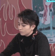 a woman in a black sweater is sitting in front of a wall with a picture of a woman on it .