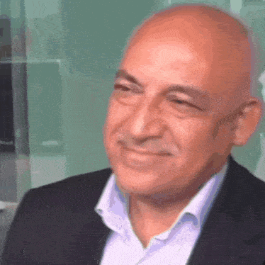 a bald man wearing a suit and white shirt smiles