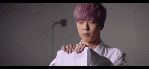 a man with pink hair is holding a piece of paper in his hands .