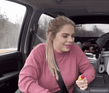 a woman wearing a pink sweater is sitting in a car