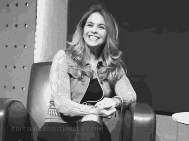 a black and white photo of a woman sitting in a chair and smiling