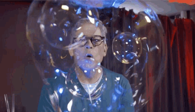 a man with glasses is blowing soap bubbles