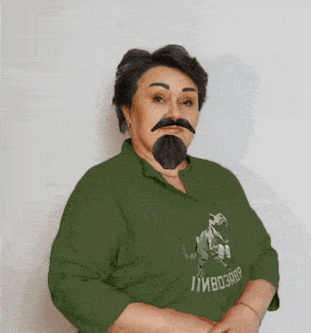 a woman with a fake beard and mustache is wearing a green shirt with a dinosaur on the front
