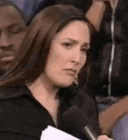 a woman is holding a microphone and making a face while sitting in a crowd .