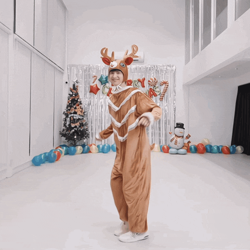 a person in a reindeer costume is dancing in front of a merry christmas banner