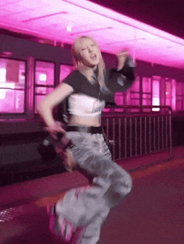 a woman in a crop top and gray pants is dancing in front of pink lights