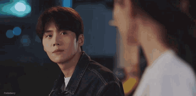 a man and a woman are looking at each other . the man is wearing a denim jacket .