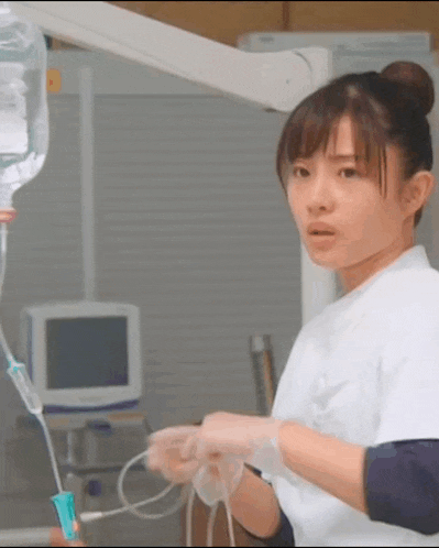 a nurse is wearing gloves and holding a syringe in a hospital .