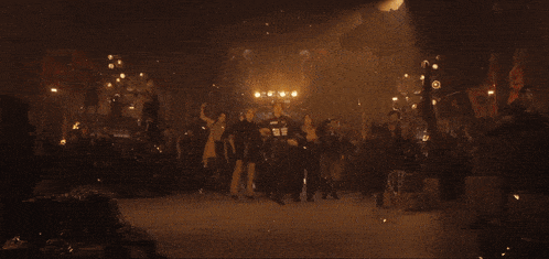 a group of people are dancing in a dark room with fire coming out of the walls