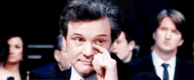 a man in a suit and tie wipes his eye with his finger