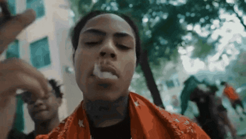 a man is smoking a cigarette in front of a crowd of people in a park .