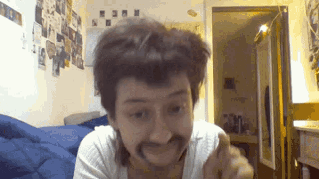 a man with a fake mustache looks at the camera in a bedroom