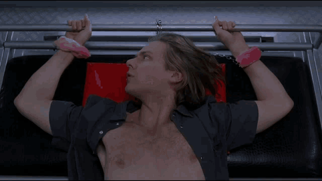 a shirtless man with pink handcuffs on his arms