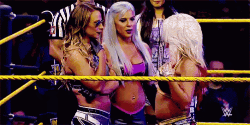 three female wrestlers are standing in a ring talking to each other .