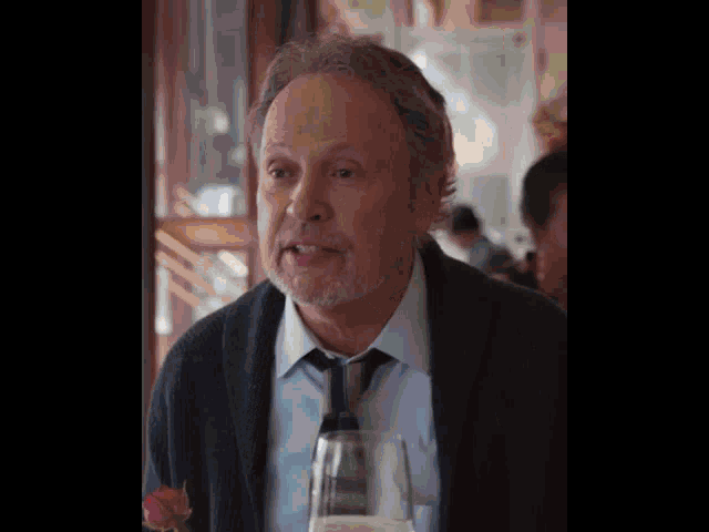 an older man with a beard is sitting at a table with a glass of wine