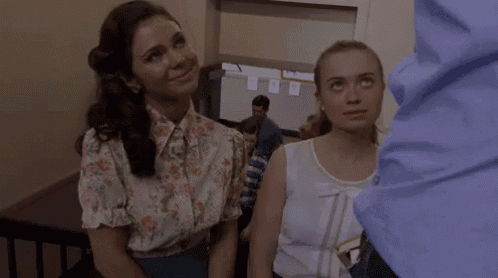 two women are sitting next to each other in a room and smiling at a man .