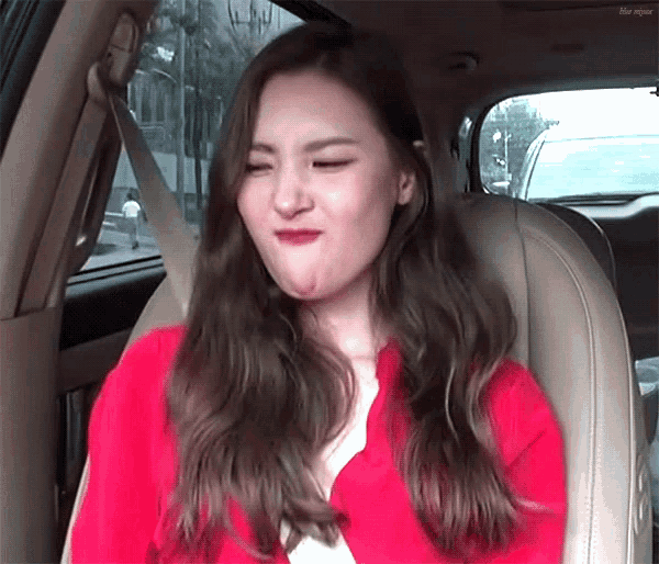 a woman in a red jacket is sitting in the back seat of a car making a funny face .