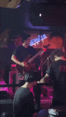 a man playing a guitar in front of a neon sign that says beyond all