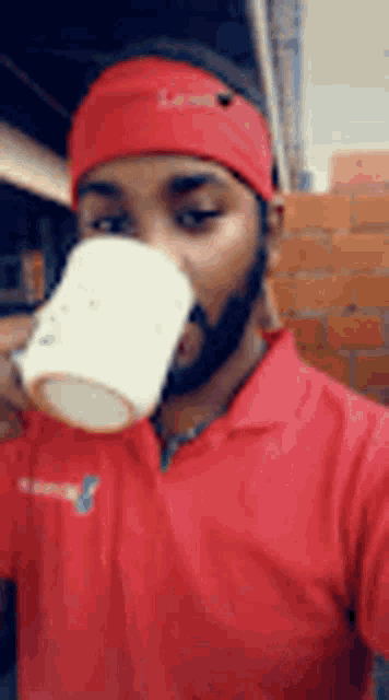 a man wearing a red shirt is drinking from a cup .