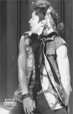 a black and white photo of a man wearing a vest and tie standing on a stage .