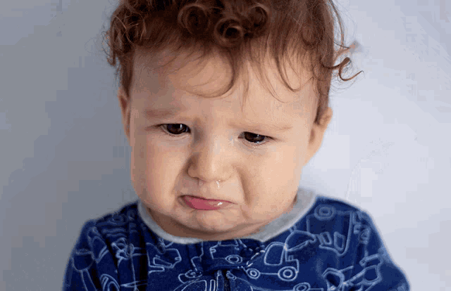 a baby wearing a blue outfit with cars on it is making a funny face