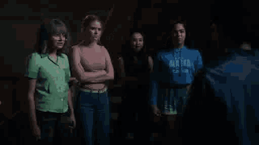 a group of girls are standing next to each other in a dark room and talking to a man .