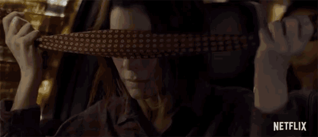 a woman in a car covering her eyes with a tie with a netflix logo behind her