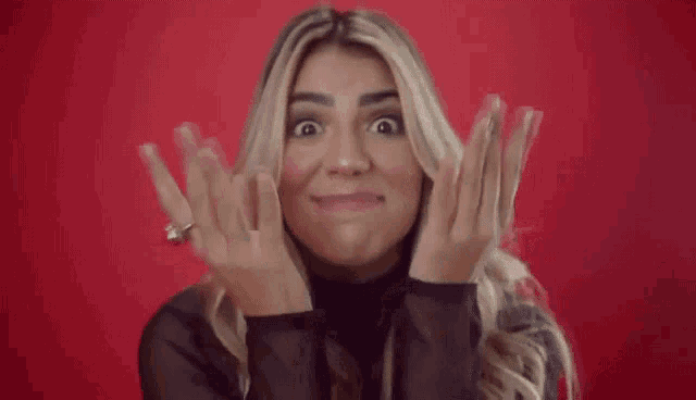 a woman is smiling and making a heart shape with her hands while wearing a ring on her finger .