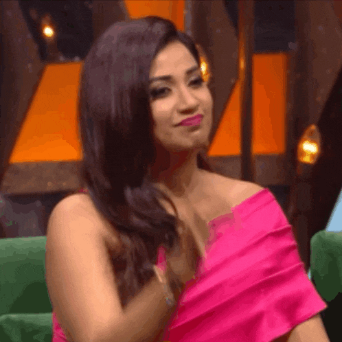 a woman in a pink dress is sitting on a green couch and holding her hair .