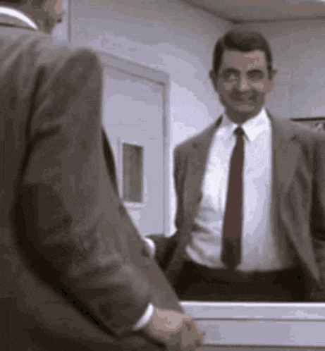 mr bean is standing in front of a mirror and smiling .