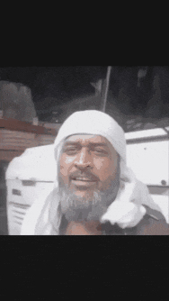 a man with a beard wearing a white head scarf giving a peace sign .