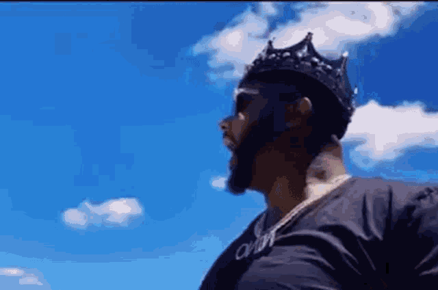 a man wearing a black crown and sunglasses is standing in front of a blue sky .