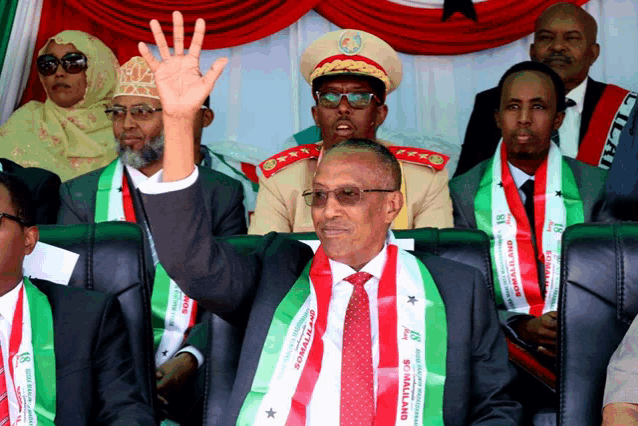 a man wearing a somaliland sash holds his hand up