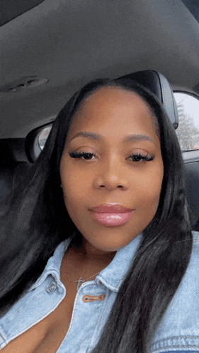a woman in a denim jacket is sitting in a car and looking at the camera