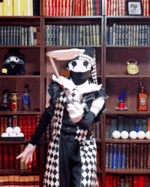 a man in a harlequin costume stands in front of bookshelves