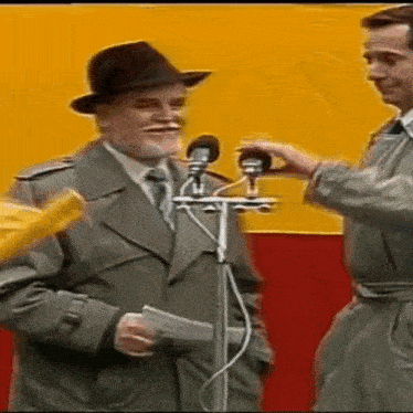 a man in a hat is standing in front of two microphones .