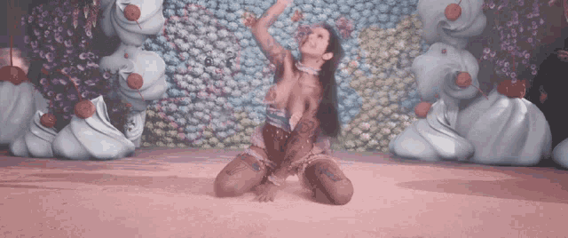 a woman is kneeling in front of a wall of flowers