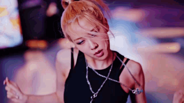 a woman wearing a black tank top and a necklace is dancing in a dark room .