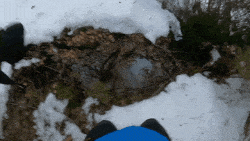 a person in a blue jacket stands in the snow near a stream