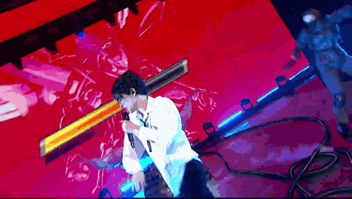 a man in a white shirt is singing into a microphone on a red stage