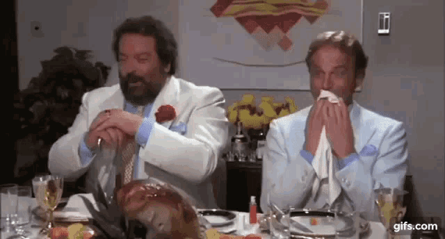 two men are sitting at a table with a turkey and a napkin in their hands .